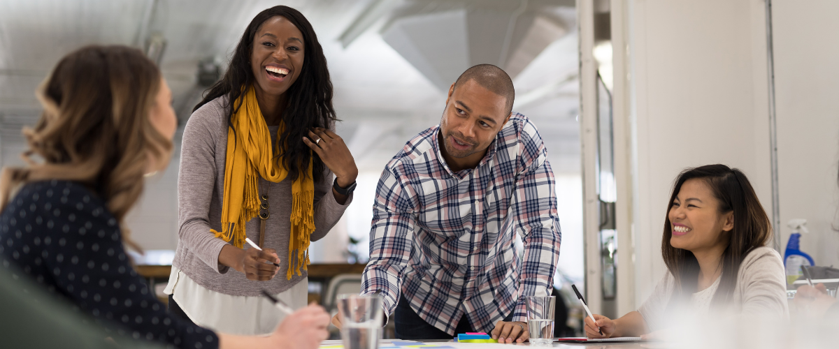 A group of PMO experts discuss strategy in an office. A woman with a yellow scarf leads the conversation