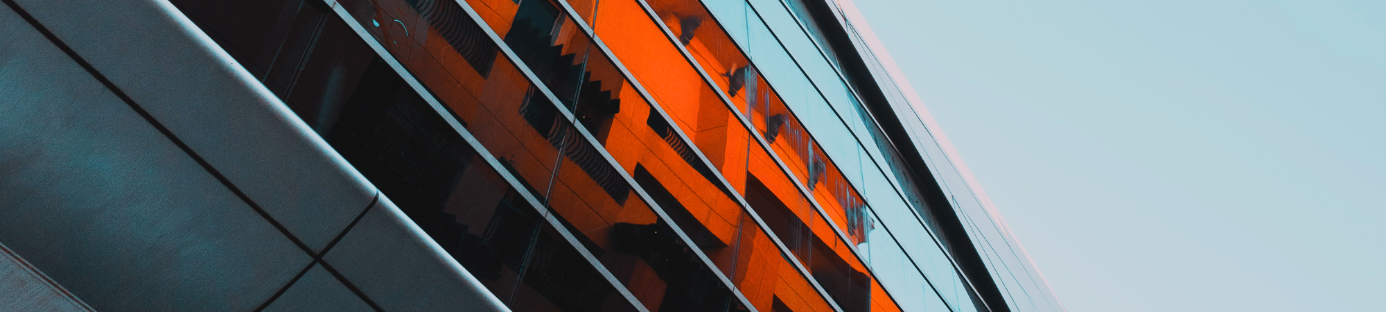 A large grey building with bright orange buildings reflected in the windows