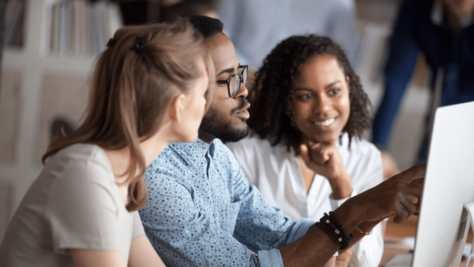 A group of product lifecycle management experts review strategy on a computer. A man points to the screen.