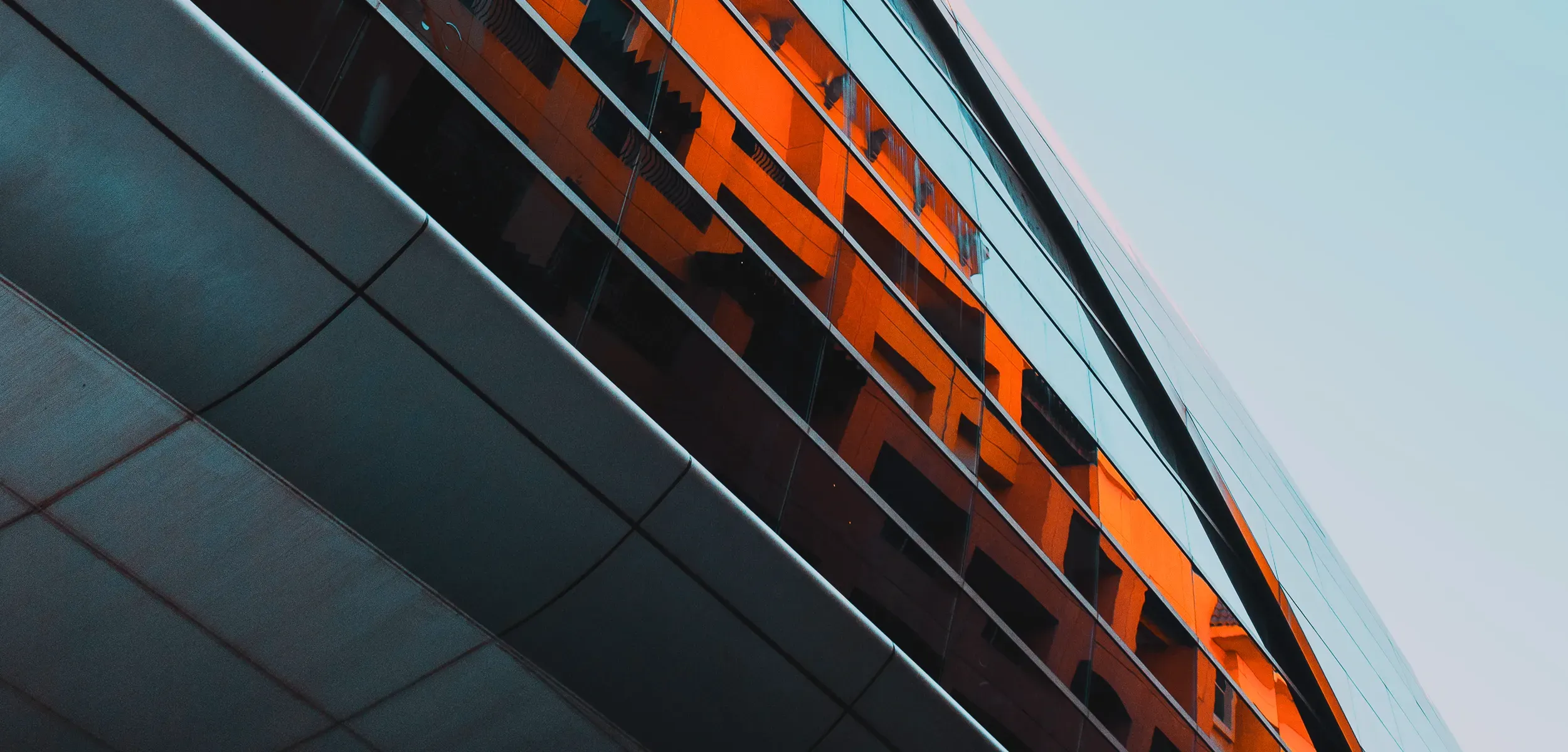 A large grey building with the reflection of bright orange buildings in the windows 